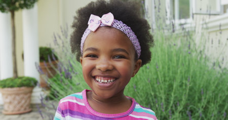 Portrait of smiling african american girl looking at camera in garden. spending time alone at home.の写真素材