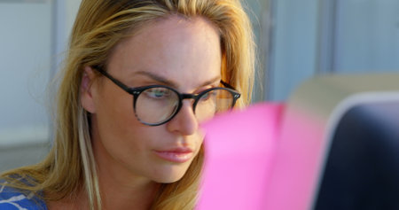 Front view of Caucasian female fashion designer working on desk in office. She is looking at computer 4kの写真素材