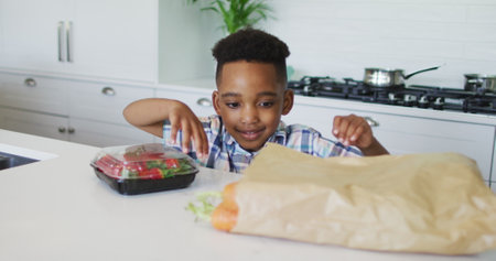 Happy african american boy unpacking groceries in kitchen. childhood, leisure and spending time at home.の写真素材