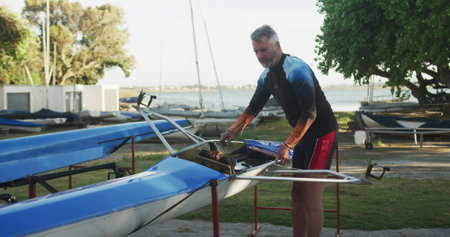 Senior caucasian man preparing rowing boat for the water. sport retirement leisure hobbies rowing healthy outdoor lifestyle.の写真素材