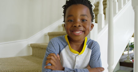 Front view close up of a cute young african american boy running down the stairs at home, sitting,...