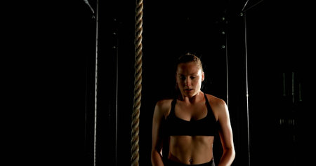 Front view of Caucasian female athlete climbing on a rope in fitness studio. She is determined and...