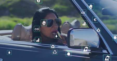 Image of eco icons over biracial woman driving car. Global green energy, environment, connections,...