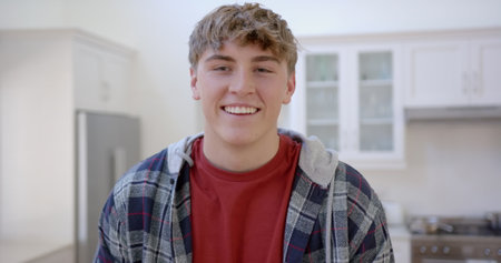 Portrait of happy caucasian male teenager with blond hair at home, slow motion. Gen z, domestic life and lifestyle, unaltered.の写真素材