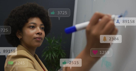 Image of icons and numbers over african american businesswoman writing in office. Global networking, business, connections, computing and data processing concept digitally generated image.の写真素材