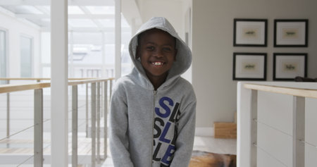 Portrait of a young African American boy at home in the sitting room, wearing a hoodie, looking at camera and laughing, slow motionの写真素材