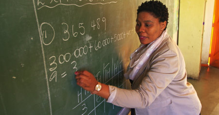 Side view close up of a middle aged African female school teacher standing at the front of the class...
