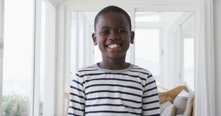 Portrait of a young African American boy at home in the sitting room, wearing a black and white striped top and smiling to camera, slow motionの写真素材