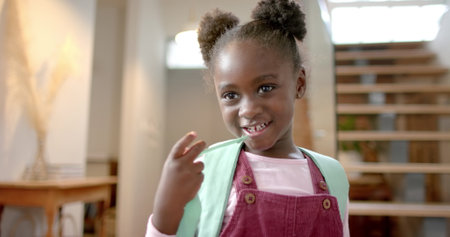 Portrait of happy african american girl with backpack at home, slow motion. Lifestyle, childhood, school, education and domestic life, unaltered.の写真素材