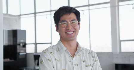 Portrait of Asian male executive standing with arms crossed in modern office. He is smiling and looking at camera 4kの写真素材