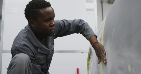 African American male car mechanic working in a township workshop, polishing a side of a carの写真素材