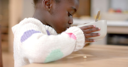 African american girl eating cereal with milk in kitchen. Healthy lifestyle, childhood, food and domestic life, unaltered.の写真素材