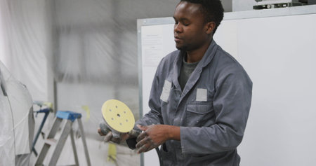 African American car mechanic working in a township workshop, checking and connecting a tool for polishing cars in slow motionの写真素材