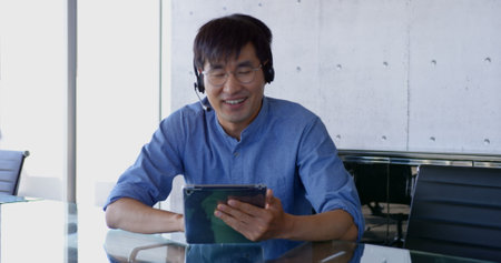 Front view of Asian male executive interacting in the office. He is sitting at desk 4kの写真素材