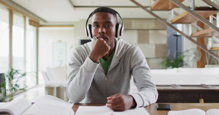 African american male teenager wearing headphones having a image conversation. at home in isolation during quarantine lockdown.の写真素材