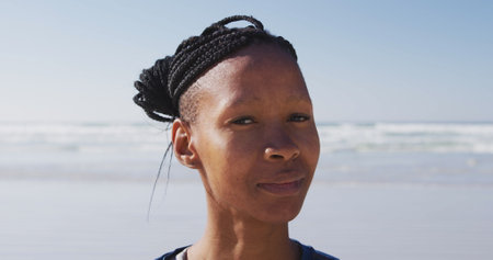 Portrait of a African American attractive woman enjoying exercising on a beach on a sunny day, practicing yoga, looking at the cameraの写真素材