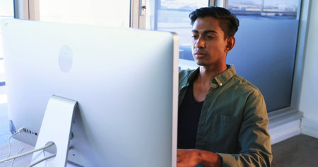 Executive using mobile phone while working on computer at desk