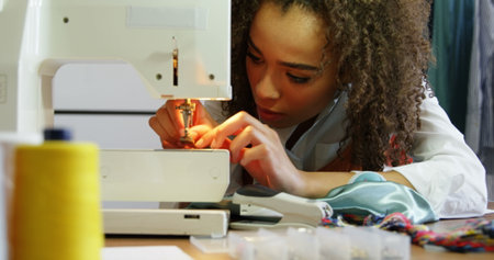 Female fashion designer working with sewing machine in workshop. She is putting thread in the sewing...