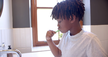 African american boy brushing teeth in bathroom at home, slow motion. Childhood, self care, hygiene and domestic life, unaltered.の写真素材