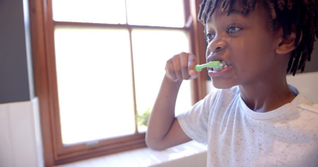 African american boy brushing teeth in bathroom at home, slow motion. Childhood, self care, hygiene and domestic life, unaltered.の写真素材