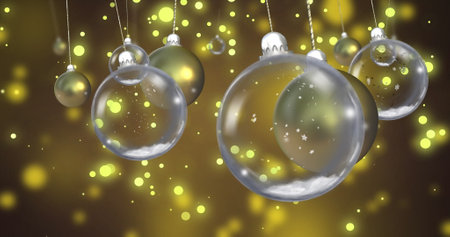 Image of glass baubles over snow falling on yellow background. Christmas, tradition and celebration concept digitally generated image.の写真素材