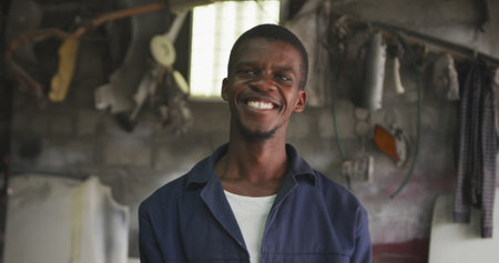 Portrait of a happy African male panel beater in a township workshop, looking at camera and smiling, slow motion. Shot in Capetown South Africa.の写真素材