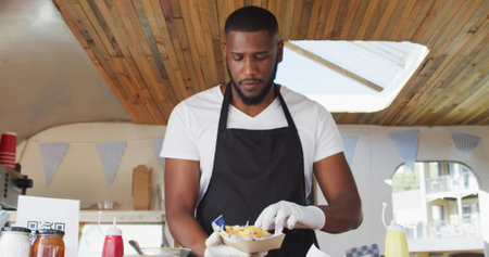 Portrait of african american man wearing apron smiling while serving food in food truck. food truck...