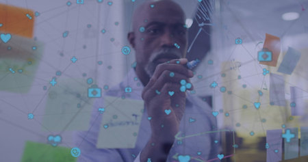 Image of network of media icons over african american casual businessman brainstorming at office....