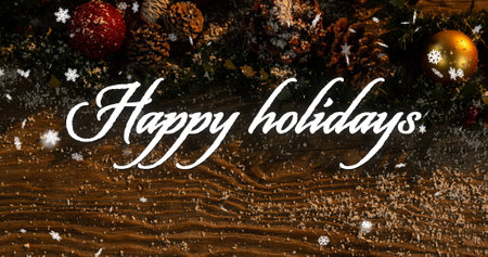 Image of happy holidays text over snow falling on christmas decorations background. Christmas, tradition and celebration concept digitally generated image.の写真素材