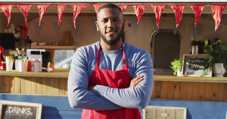 Portrait of african american man with arms crossed smiling while standing near the food truck. food truck and street food conceptの写真素材