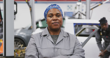 Portrait of an African American female car mechanic working in a township workshop, crossing her arms and looking at the camera in slow motionの写真素材