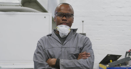 Portrait of an African American male car mechanic working in a township workshop, crossing his arms and looking at the cameraの写真素材