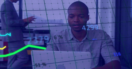 Image of financial data processing over african american businessman using laptop in office. Global finance, business, connections, computing and data processing concept digitally generated image.の写真素材