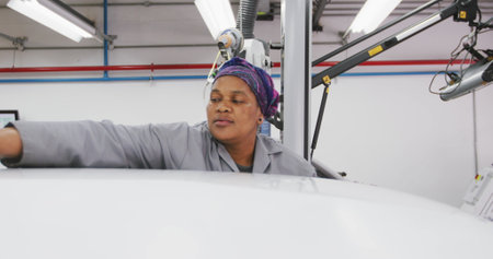 African American female car mechanic working in a township workshop, cleaning the roof of a car with a rag in slow motionの写真素材