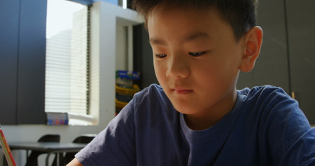 Front view of attentive Asian schoolboy studying at desk in classroom at school. He is writing on notebookの写真素材