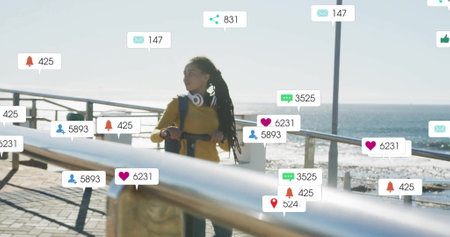Social media notifications image over woman walking along seaside promenade. technology, smartphone, digital, connection, lifestyle, outdoorsの写真素材