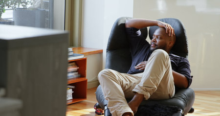 Front view of African american man relaxing on chair in a comfortable home. He is looking awayの写真素材