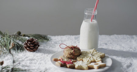 A festive table features cookies and milk, evoking holiday cheer. Pine branches and a pinecone add a natural touch, highlighting the season's traditions.の写真素材