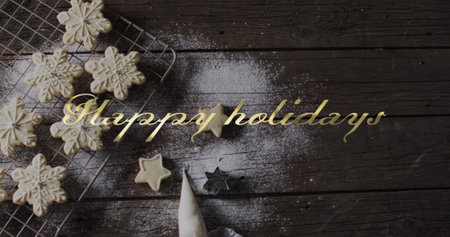 Happy holidays text win gold over snowflake christmas cookies on dark wood. Christmas, new year, tradition, greetings and celebration digitally generated image.の写真素材