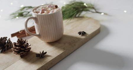A mug of hot chocolate sits on a wooden board, evoking a cozy atmosphere. Pine cones and star anise add a festive touch, suggesting holiday warmth and comfort.の写真素材