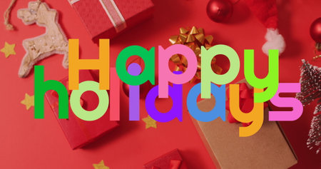 Image of happy holidays text banner over christmas decoration and gifts on red background. Christmas festivity and celebration conceptの写真素材
