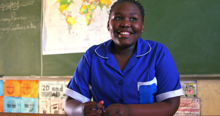Smiling student in blue uniform sitting at desk in classroom, feeling happy. Education, learning, study, lesson, happiness, joyの写真素材