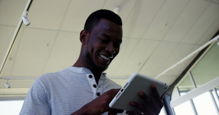 Smiling man using tablet in modern office, enjoying digital content. Technology, business,...