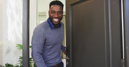 Smiling man opening front door, welcoming guests into cozy home. Hospitality, welcome, invitation,...