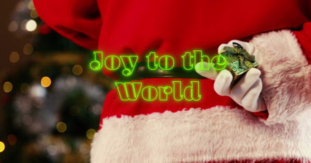 Image of neon green joy to the world text banner over santa claus decorating a christmas tree. Christmas festivity and celebration conceptの写真素材