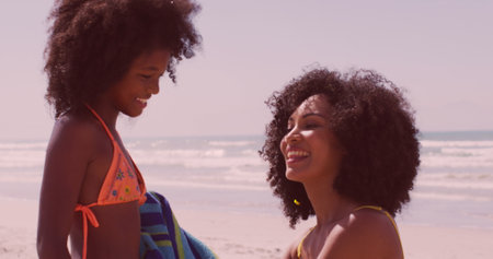 Young biracial woman and African American girl share a joyful moment on the beach. Their smiles radiate warmth, capturing a carefree day by the sea.の写真素材