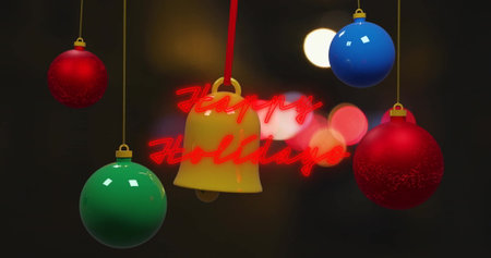 Image of happy holidays text with colorful baubles and bell hanging over lens flare. Digital composite, decoration, lights, christmas festivity, winter holiday and celebration concept.の写真素材