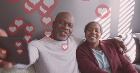 Image of hearts over senior african american couple taking selfie at christmas. Christmas tradition and celebration concept digitally generated image.の写真素材