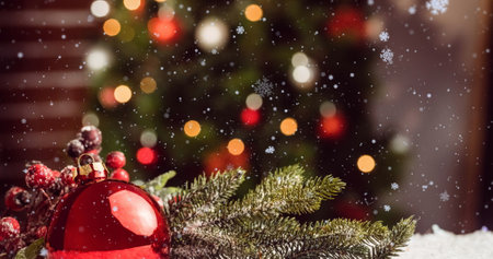 Image of snowflakes over bauble decoration against blurred view of christmas tree at home. Christmas festivity and celebration conceptの写真素材