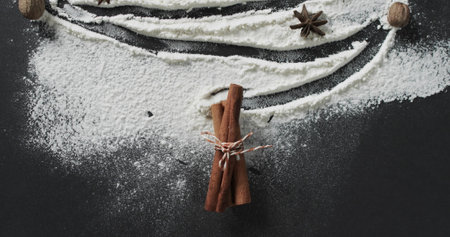 Cinnamon sticks tied with string lie amidst flour on a dark surface. Ingredients are artistically...